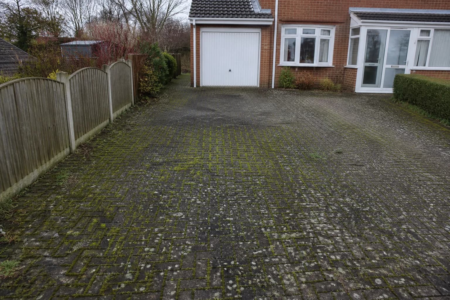 A Greater Manchester block paving driveway covered in moss, black lichen and weeds before cleaning